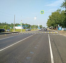Photographie d'une route au niveau d'un passage piéton, avec une station-essence à droite.