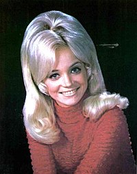 A bust of Barbara Mandrell, who is wearing a red sweater and smiling.