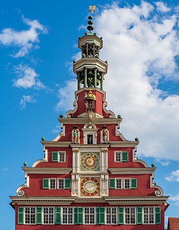 Esslingen am Neckar: frontão norte da Altes Rathaus (Antiga Prefeitura) com o topo da torre do relógio astronômico e o carrilhão. Com a reinstalação, em janeiro de 2007, do relógio histórico de 1589, a cidade tem o único e o mais antigo relógio de torre de ferro forjado em funcionamento na Alemanha. Na maior parte, o relógio consiste em peças originais de 1595. O acionamento é fornecido por três pesos ​​de arenito. Os pesos são levantados eletricamente — caso contrário, o relógio teria que ser enrolado à mão diariamente. Em Esslingen, o carrilhão é composto por 29 sinos e começa a tocar às 12 horas. (definição 5 149 × 5 149)