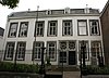 Door een gebroken kap afgedekt huis met brede lijstgevel Op het achterterrein resten van de 13e-eeuwse stadsmuur