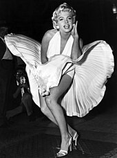 Monroe is posing for photographers, wearing a white halterneck dress, which hem is blown up by air from a subway grate on which she is standing.