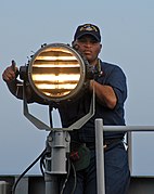US Navy sailor sending Morse code using a signal lamp.