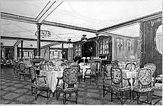 Pemandangan restoran berpanel kayu hias. Meja dengan empat atau lima kursi bantal terlihat di seluruh gambar, dengan celemek gulung dan lampu meja diletakkan di atas meja.