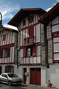 Photographie de façades de maisons basques, aux pans de bois rouge sang, avec une garée en premier plan.