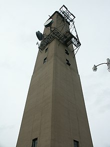 Early stations, like this one near Valparaiso, Indiana, were built of concrete. They housed the electronics mid-way up the tower, behind the window-like openings, to avoid line losses. These were replaced by the steel framework towers as the cost of steel dropped through the 1950s. ValpoTower1.JPG