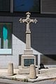 Photo en couleur d'une croix commémorative en pierre au pied d'un bâtiment.