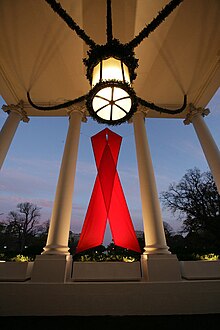 A large red ribbon hangs between columns in the north portico of the White House for World AIDS Day, November 30, 2007. WHredribbonNorthPortico.jpg