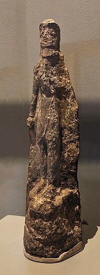 Figurine-plaque en terre cuite peinte, représentant un personnage debout, sans doute Gilgamesh, piétinant la tête de Humbaba après l'avoir vaincu. Début du IIe millénaire av. J.-C., Tell Asmar (?), Musée du Louvre.