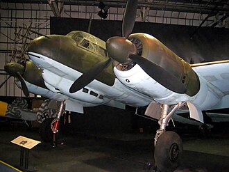 Una fotografía en color de la sección frontal de un avión de hélice bimotor en un museo, que se muestra en semi perfil, visto desde la parte frontal izquierda.  El avión está pintado de verde y azul claro.  Las antenas sobresalen del morro del avión.