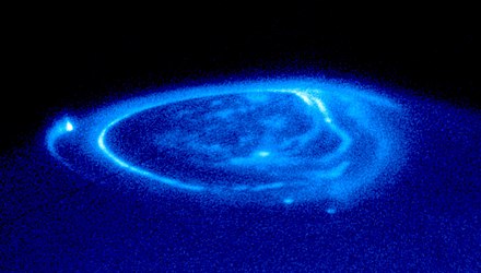 Aurora di Jupiter. Tiga titik yang cerah dihasilkan oleh tabung fluks magnetik yang terhubung dengan satelit Io (di kiri), Ganimede (bawah), dan Europa (juga di bawah). Wilayah yang sangat terang dan hampir berbentuk bulat (yang disebut oval utama) dan aurora kutub yang lebih redup juga dapat terlihat.