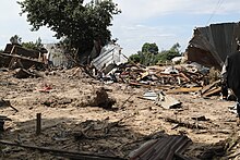 Blick auf eine durch eine Schlammlawine zerstörte Reihe von Hütten. Links ragt ein Dach und ein Baum heraus und rechts sind Überreste einer Blechhütte zu erkennen.