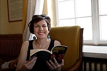 Woman smiling while sitting, holds her book of poetry near the window