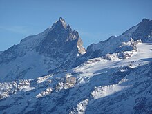 Utsikt over en omtrent pyramideformet og tagget topp i et miljø med snø og is.