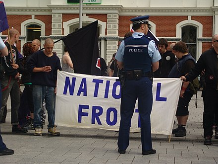 Police officer in New Zealand with chequered band on hat and stab vest NZ NF counter-protest.jpg