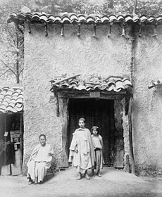 One Arab man and two Arab children in front of Kabyle house.jpg