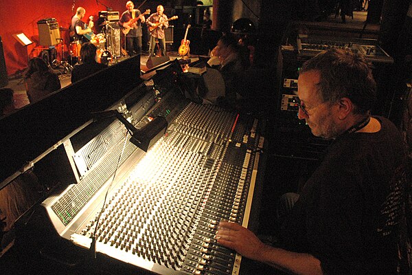 An audio engineer adjusts a mixer while doing live sound for a band.