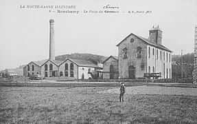 Fotografía en blanco y negro que muestra un grupo de naves industriales, una de las cuales es muy alta y alberga el cabecero, este último sobresale, coronado por un campanario de madera.  A la izquierda hay una gran chimenea.