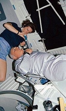 Scientists and astronauts Kathryn D. Sullivan and Bruce McCandless I are performing medical studies on Central Venous Pressure and associated drug-related studies. STS-31 MS Sullivan, MS McCandless, DSO 462 medical device on OV-103 middeck.jpg