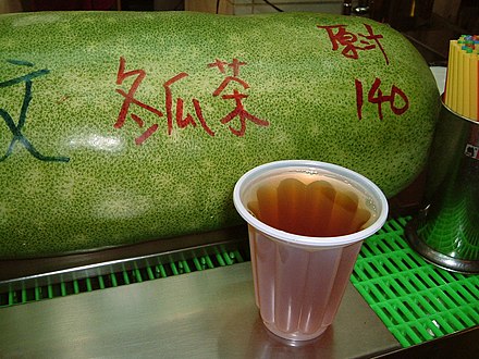 A cup of winter melon punch in front of a winter melon at a Taiwanese street vendor's stall