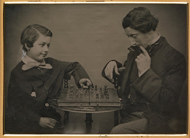 An old timey photo of a man and boy playing chess.