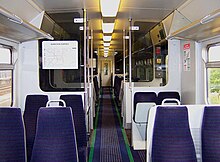 Photograph taken inside the train. There are seats on both sides. There is a gap in between for people to stand and for doors to open. The floor is blue with green borders.