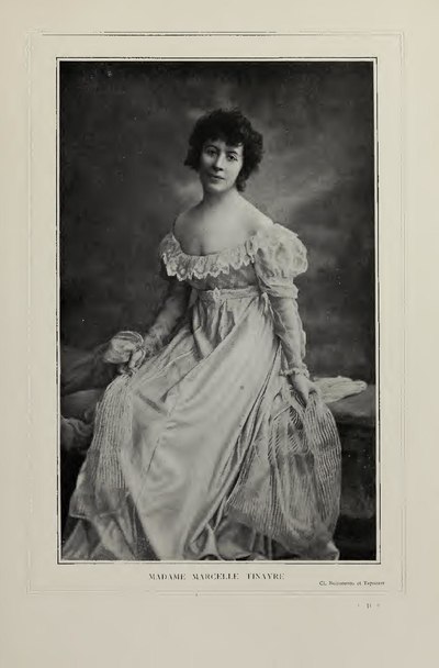 Madame Marcelle Tinayre, photographie assise sur une banquette en robe claire à dentelle.