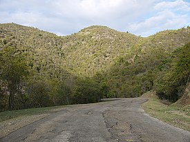 photo of a paved road, with crumbling pavement, and 3 hills in the distance