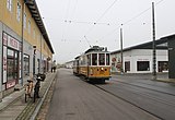 Motorwagen KS 327 (bouwjaar 1912) in de Valby Langgade, de 'Hoofdstraat' van het museum. Langs deze straat is een stedelijke sfeer gemaakt door de aankleding met winkels, waaronder de mejeri of ismejeri (links), dit was een melkwinkel.