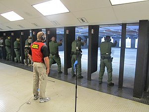 An indoor shooting range for American federal law enforcement personnel. A rangemaster is shown supervising typical firearms training exercises. Federal law enforcement officers during firearms training exercises at indoor firing range.jpg