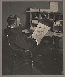 John Philip Sousa seated at a desk and looking at "The Invincible Eagle March" sheet music