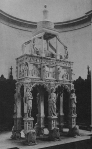 Photographie en noir et blanc d'une structure en pierre comprenant de bas en haut des cariatides, un sarcophage aux parois sculptées, un gisant et une statue.