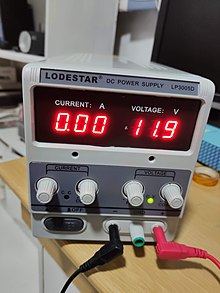 D.C. variable bench power supply unit, with a digital display showing current (left) and voltage (right), and three banana connectors (+, ground, -). Other power supplies may use the opposite order for indicators and connectors, and two different colours for the indicators. Bench power supply.jpg