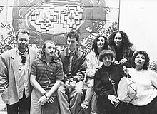 Black and white photograph of seven people, variously sitting and standing, in front of a wall with a geometric bas relief.