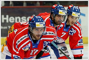 Kleurenfoto van drie ijshockeyspelers die naar rechts kijken