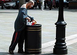 Homme fouillant une poubelle à Londres pour y trouver de la nourriture.