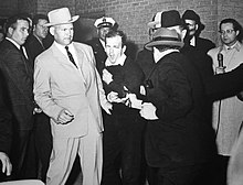 Jack Ruby shooting Oswald, who was being escorted by police detective Jim Leavelle (tan suit) for the transfer from the city jail to the county jail. Ruby shoots Oswald.jpg
