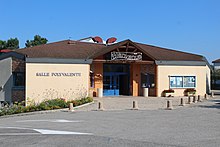 Bâtiment à toit marron et façade beige sur laquelle est inscrit "Salle polyvalente".