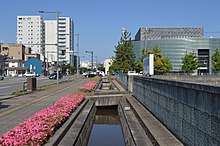 福井県福井市を流れる芝原用水（芝原上水）。右前は福井県国際交流会館。 （福井市、北緯36度4分1.58秒 東経136度13分35.09秒﻿ / ﻿北緯36.0671056度 東経136.2264139度﻿ / 36.0671056; 136.2264139﻿ (福井市を流れる芝原用水)）