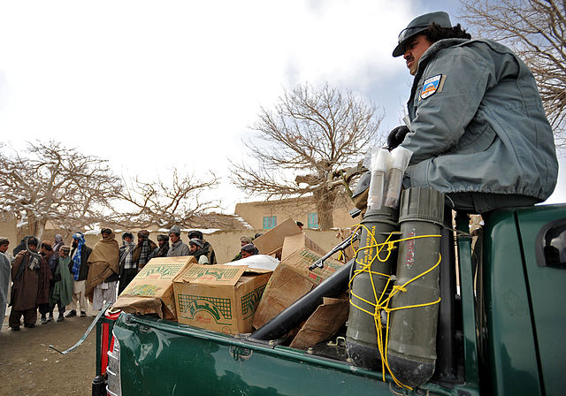 An Afghan National Police officer, right, stands watch over food before distributing it to families Feb. 5, 2012, in Pinzo village, Zabul province, Af