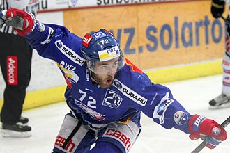 Farbfoto eines Eishockeyspielers, der sich bückt und seine Arme zum Himmel hebt