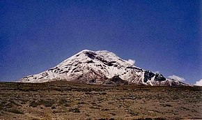 A snow-capped mountain lies in the distance against a cloudless blue sky. The land in the foreground is very barren.