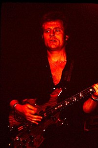 A red-tinged photograph of John Paul Jones playing an 8-string bass guitar in concert