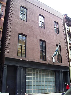 A three story brick building whose lowest floos is painted black with a large frosted glass and silver metal window takign up most of the street frontage.