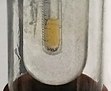 A glass tube, is inside a larger glass tube, has some clear yellow liquid in it