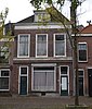 Winkelwoonhuis, in het midden van de 19de eeuw gebouwd in een sobere eclectisch-classicistische trant, pui uit het einde van de 19de eeuw.