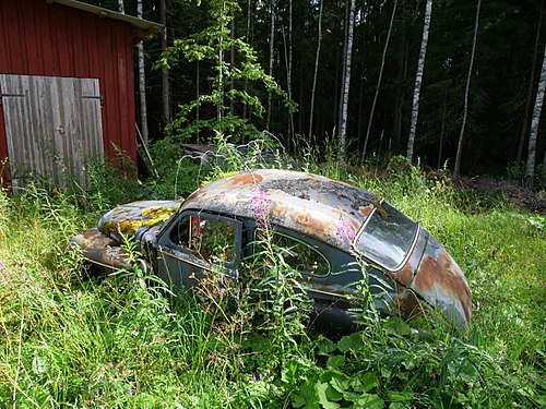 Rusty car next to a way in a swedish forest.