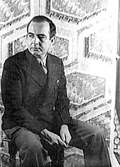 черно-белая фотография Сэмюэля Барбера в полный рост, сидящего на три четверти длины и поворачивающего голову влево.