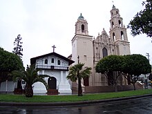 The original Mission San Francisco de Asis adobe structure is the smaller building at left, while the larger structure is a basilica completed in 1918 (the architectural style was influenced by designs exhibited at San Diego's Panama-California Exposition in 1915). San Francisco de Asis--Mission Dolores.JPG