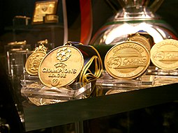 Front three: Manchester United's treble medals of the 1998-99 season are displayed at the club's museum. The Champions League Winners Medal (Manchester United Museum) (262769292).jpg