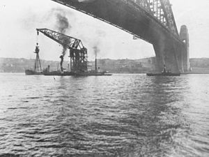 Floating crane Titan, yang ditarik di bawah Sydney Harbour Bridge dengan tiang dari HMAS Sydney di tahun 1929. Tiang akan dipasang di Bradleys Head, New South Wales.